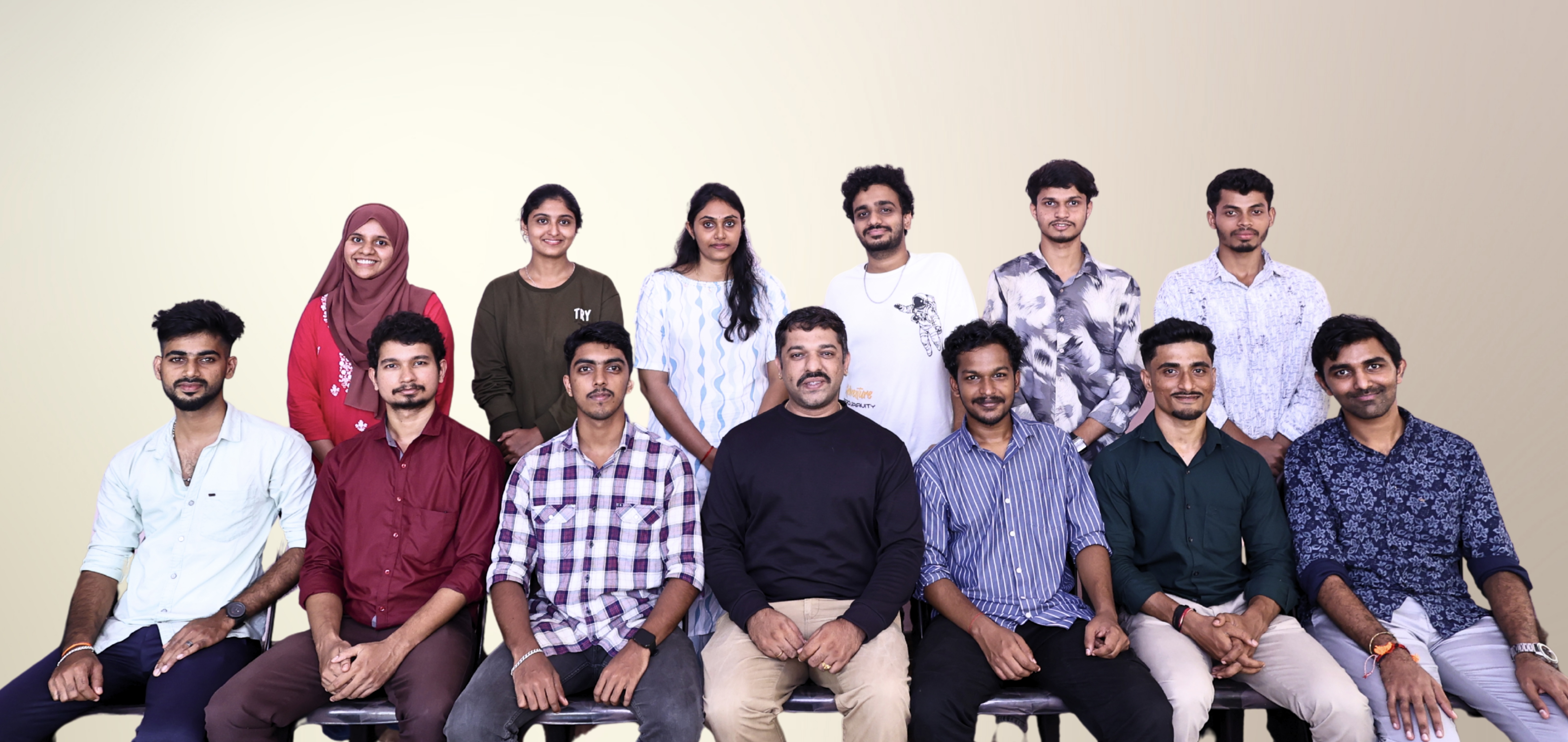 A group of seven colleagues smiling for a photo in front of a decorative wall with bookshelf motifs.